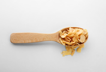 Dried garlic flakes in spoon on white background