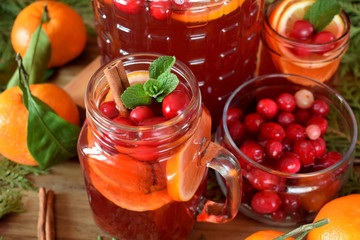Punch with cranberries and orange decorated with mint and a stick of cinnamon in glass vessels
