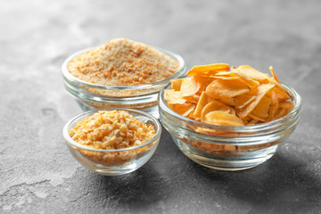 Dried garlic flakes, granules and powder in glass bowls on grey background