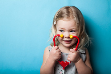 European little girl with toy stethoscope in hands on a blue background. © Andrii Zastrozhnov