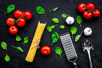 Italian pasta concept. Spaghetti, tomatoes, garlic, cheese grater, spoon for spaghetti on black background top view