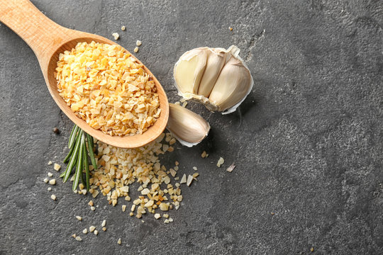 Wooden spoon with granulated dried garlic on grey background
