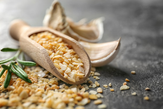 Wooden scoop with granulated dried garlic on grey background