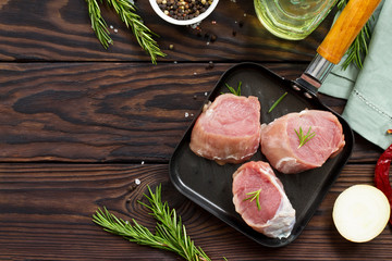 Fresh meat. Raw pork steak on a cast iron frying pan, spices and fresh rosemary on a kitchen wooden table. Flat lay. Top view with copy space.