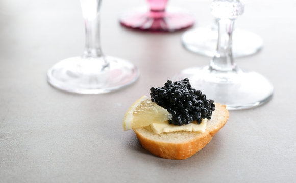 Tasty sandwich with black caviar and lemon on table