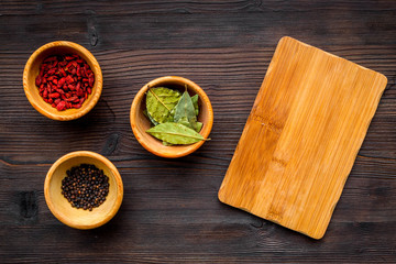 Make menu or write recipe. Mock up for menu or recipe. Wooden cutting board near ingredients in bowls bay leaf, black repper and godji on dark wooden background top view