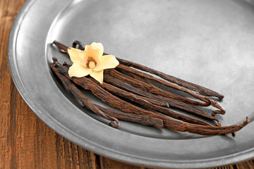 Metal plate with vanilla sticks and flower on wooden background