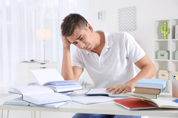 Stressed student preparing for exam at table indoors