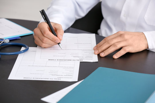 Doctor filling in insurance form at table