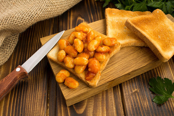 Toast with  beans in tomato sauce on the  wooden cutting board