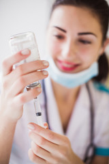 Close-up the cheerful young nurse who is dialing medicine into the syringe indoors