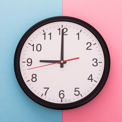 Big wall clock isolated on blue and rose background. Nine o'clock.