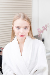 portrait of attractive smiling woman blond. In a white bathrobe after the procedure. Cosmetology and SPA center concept.