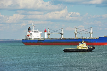 Naklejka premium Tugboat assisting bulk cargo ship