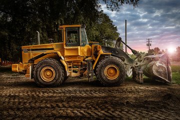 Large bulldozer at construction site, cloudy sky and sunset in background.
