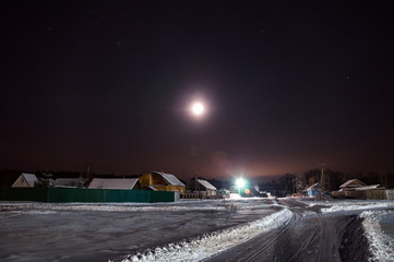 Fototapeta na wymiar Snow-covered road on a winter night . Around the silence and the starry sky with a moon halo.