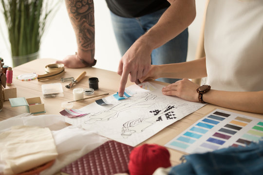 Fashion designers team choosing colors for new collection discussing sketches, dressmakers working on clothes creation using swatches pallet, teamwork in design studio concept, close up view