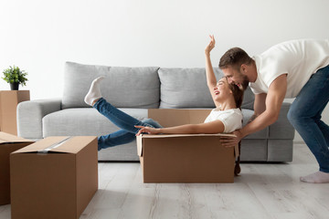 Happy couple having fun laughing moving into new home, young excited woman riding sitting in...