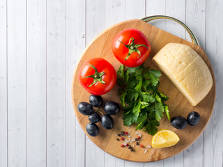 Piece of cheese with parsley, tomatoes grapes on a cutting Board.