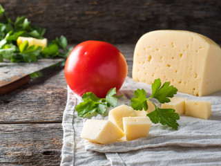 Piece of cheese with parsley, tomatoes on a linen towel Rustic wooden background