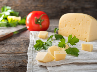Piece of cheese with parsley, tomatoes on a linen towel Rustic wooden background