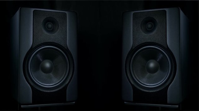 Set of two black round audio speakers vibrating from sound of loud music on low frequency. Modern sub-woofers on black background.