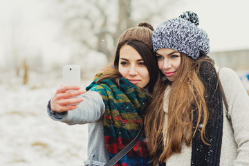 Two female teenage girl friends in winter taking a selfie on smart phone