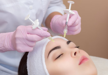 Obraz na płótnie Canvas The doctor cosmetologist makes the Rejuvenating facial injections procedure for tightening and smoothing wrinkles on the face skin of a beautiful, young woman in a beauty salon.Cosmetology skin care.