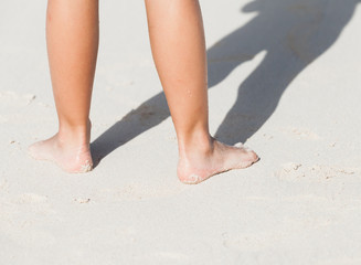 Wet female feet stand on white coastal sand