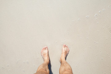 Male feet stand on white sand, top view