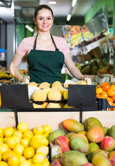 smiling attractive salesgirl standing near fresh fruits and vegetables in store