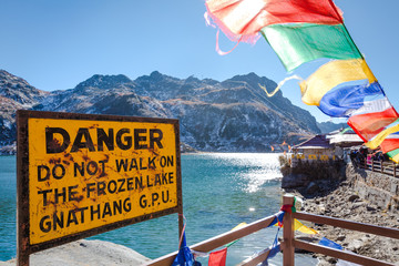 Tsomgo lake / Changu lake near Gangtok city in East Sikkim, North east India. Beautiful Buddhist prayer flags flutter and danger sign board in front of lake.  Colorful wallpaper for Travel & Tourism