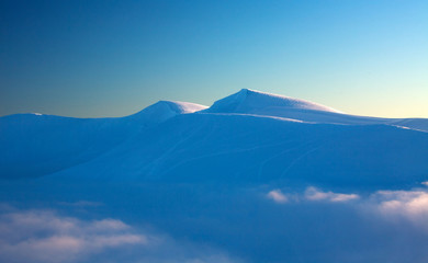 Sunset on top of snowy winter mountains on sky background
