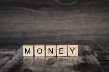 the word money made of bright wood cubes with black letters on a dark wooden background