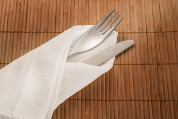Fork and knife into white textile on bamboo background