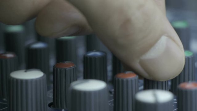 Close-up of male fingers turning equalizer knobs on audio mixing desk. Shot with multiple equalizer and fader knobs.
