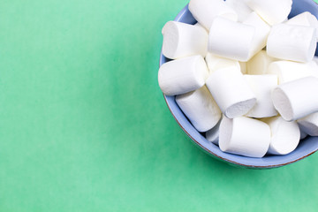 Marshmallows in blue plate on pastel green background.