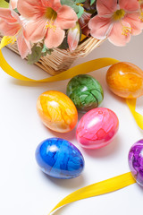 Bunte Ostereier und gelbes Band mit dekorativen Blumen im Korb.