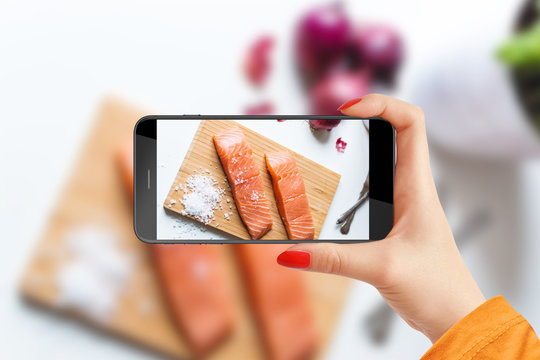 Girl taking picture of salmon slices on wooden plate with her phone