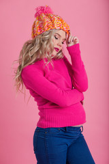 Beautiful happy pregnant woman is wearing warm winter clothes hat and sweater isolated on pink background