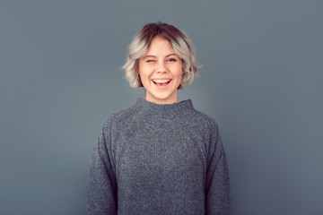 Young woman in a grey sweater studio picture isolated on grey background wink