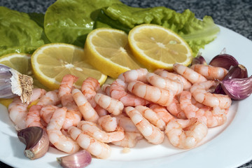 peeled king prawns with lemons, garlic and salad on plate