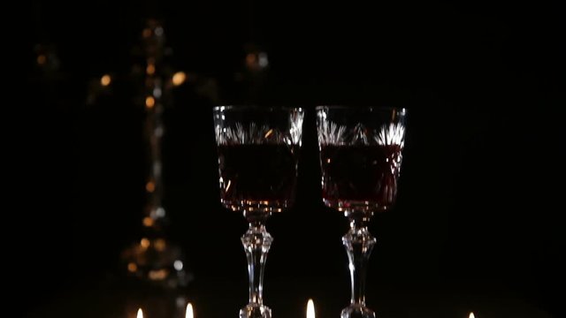 Two glasses of wine on black background and burning candles..Glasses of red wine over candlelight and darkness..Slider video footage.Romantic evening with wine.
