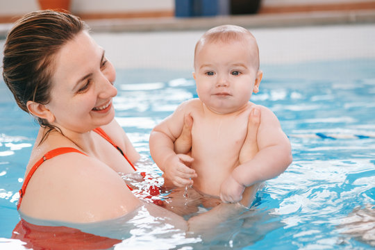White Caucasian mother traning her newborn baby to float in swimming pool. Baby diving in water. Healthy active lifestyle. Family activity and early development concept
