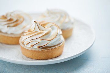 Obraz na płótnie Canvas Delicious lemon tartlets with meringue on a white vintage plate. Sweet treat on a light blue background