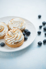 Delicious lemon tartlets with meringue on a white vintage plate. Sweet treat on a light blue background