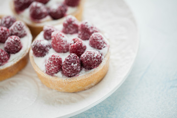 Delicious raspberry tartlets on a white vintage plate. Sweet treat on a light blue background