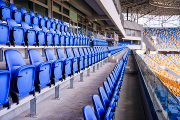 Empty blue plastic chairs in a row at the football stadium. - obrazy, fototapety, plakaty