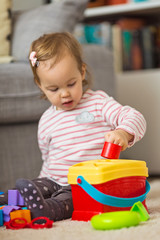 Two years old toddler girl playing on the floor, putting plastic shapes into the box with appropriate holes