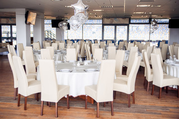 Obraz na płótnie Canvas Serving a festive round table decorated with white elegant chairs and decorated with balloons for a festive dinner.